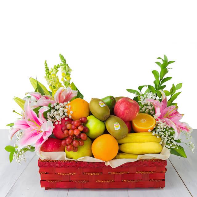 Keranjang buah segar dengan bunga lili pink, buah-buahan, dan dedaunan hijau — online florist terpercaya