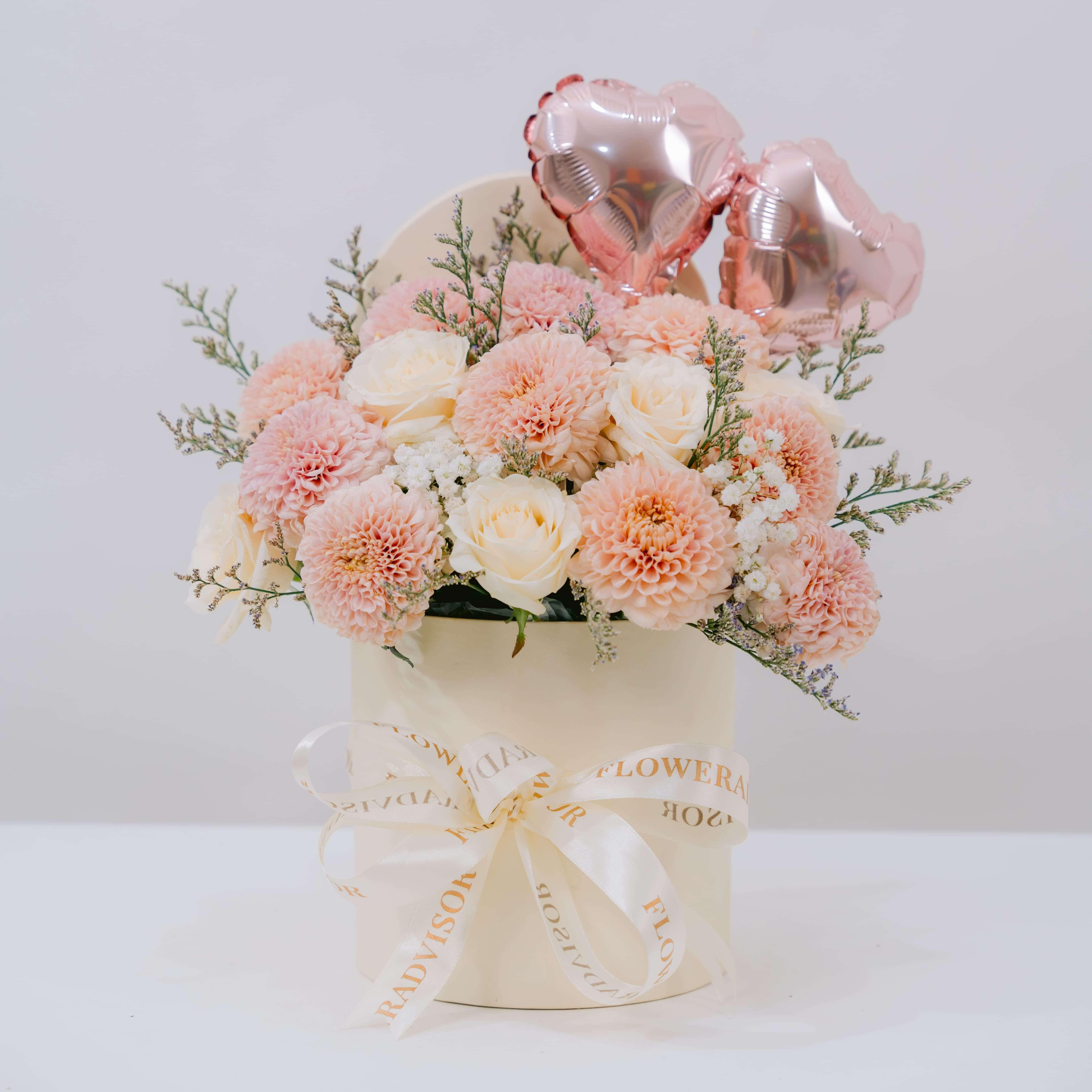 Floral arrangement in a box with pink balloons on a white background
