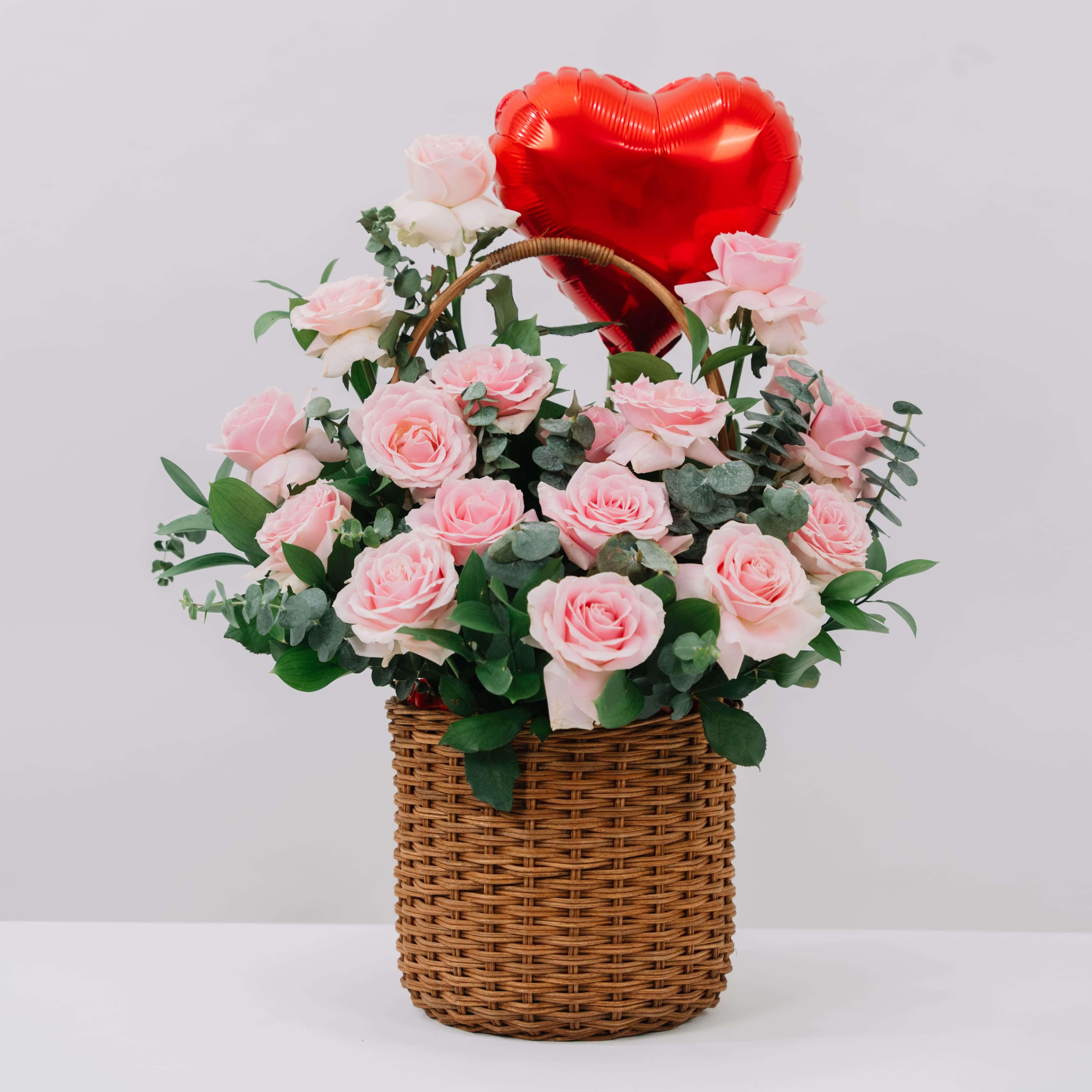 Bunga mawar pink dalam keranjang anyaman dengan balon hati merah, online florist