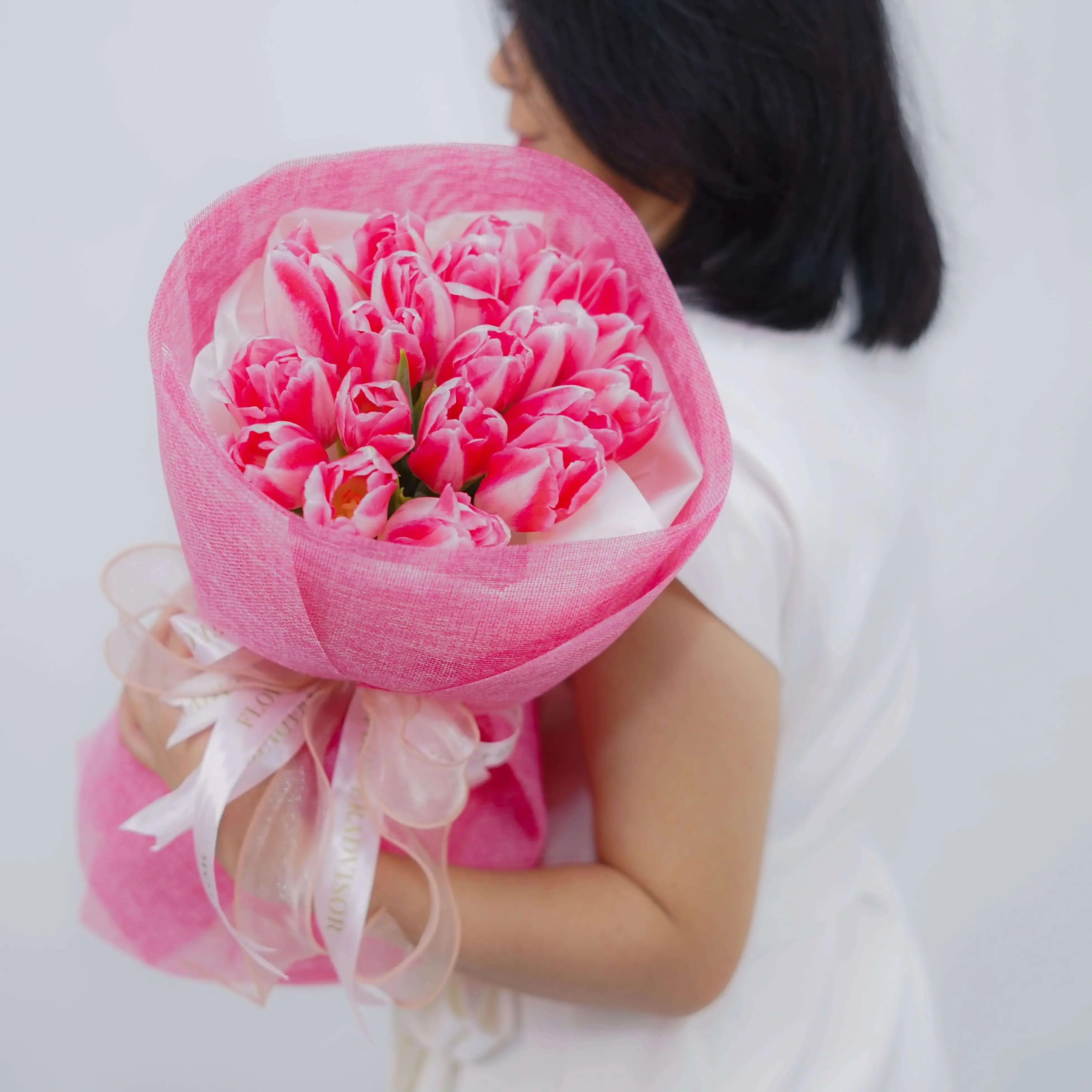 Bouquet bunga tulip pink cantik, dibungkus kain jaring pink dan pita, dari online florist terpercaya.