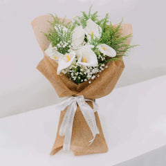 Buket bunga calla lily putih dan baby's breath, dikemas rapi dengan kain anyaman, dari online florist