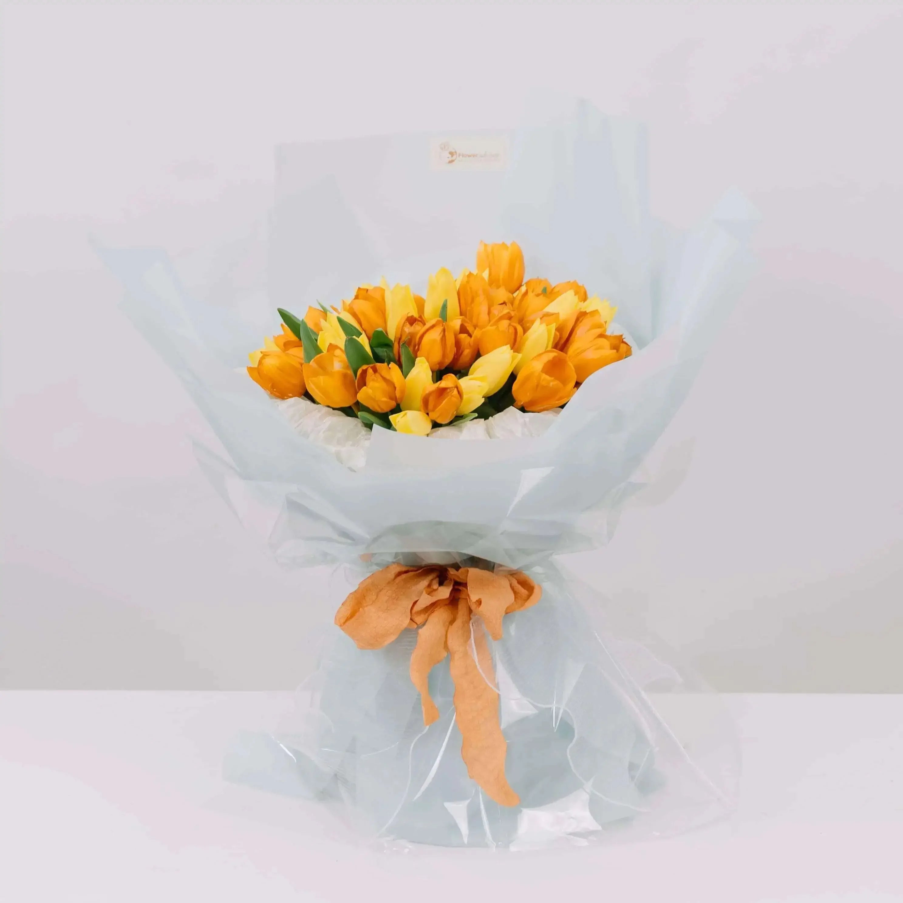 Buket tulip kuning dan oranye dari online florist, dibungkus kertas biru muda dengan pita oranye
