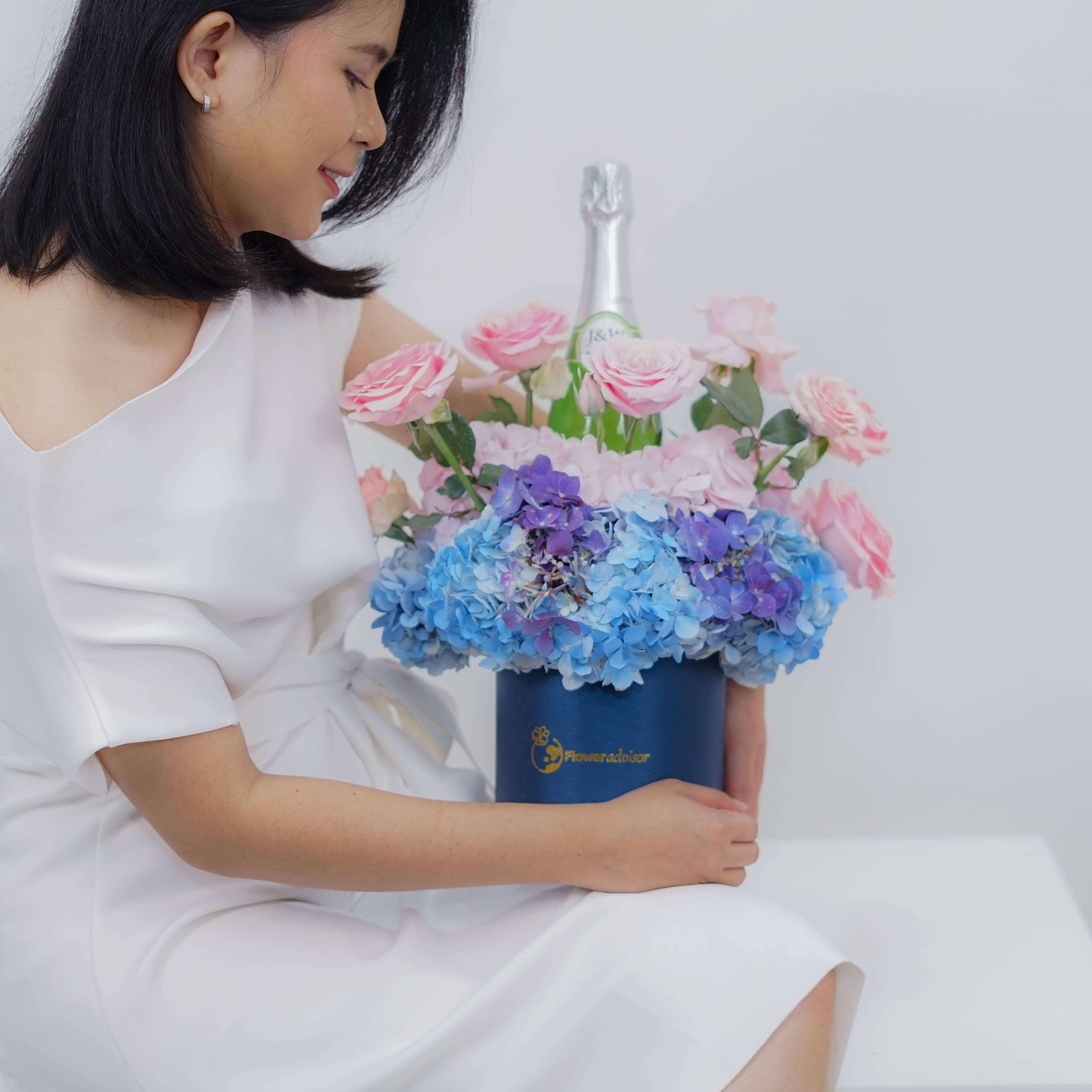 Wanita tersenyum memegang rangkaian bunga mawar pink dan hortensia biru dari online florist