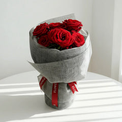 Buket bunga mawar merah segar, dikemas rapi dengan kertas abu-abu dan pita merah. Online florist terpercaya.