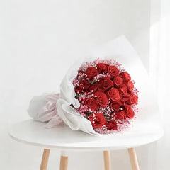 Buket bunga mawar merah segar dari online florist, dibungkus kertas putih dan pita pink, siap dikirim.